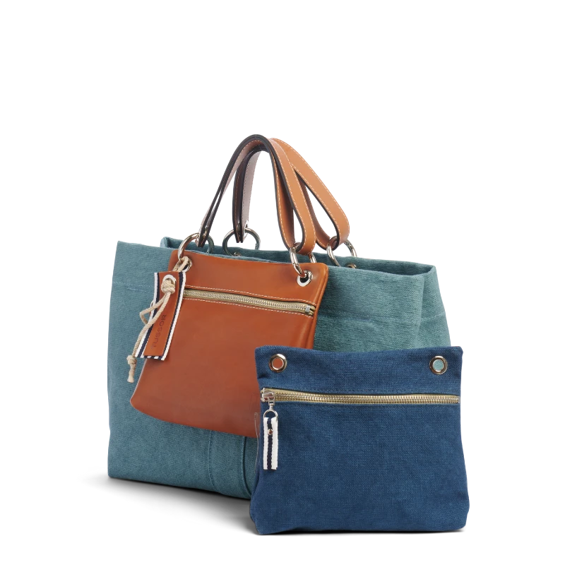 sac de ville modulable en coton bleu français avec des anses en cuir naturel avec des dossiers et sa pochette yole bleu français sur un canapé
