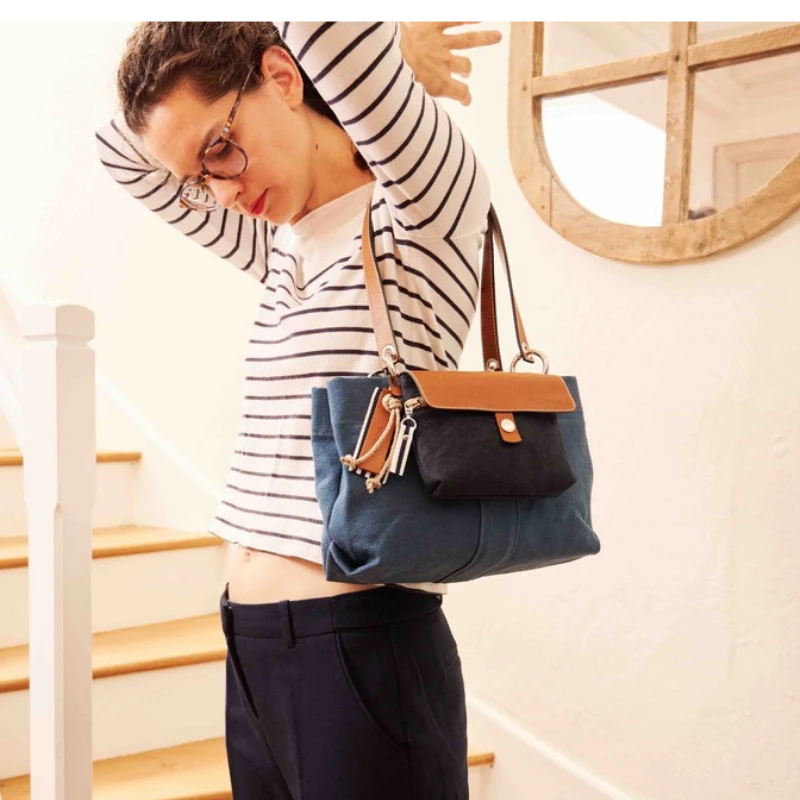 sac de ville modulable en coton bleu canard avec des anses en cuir naturel avec sa mobile marine tenu par ne femme en tee shirt marin