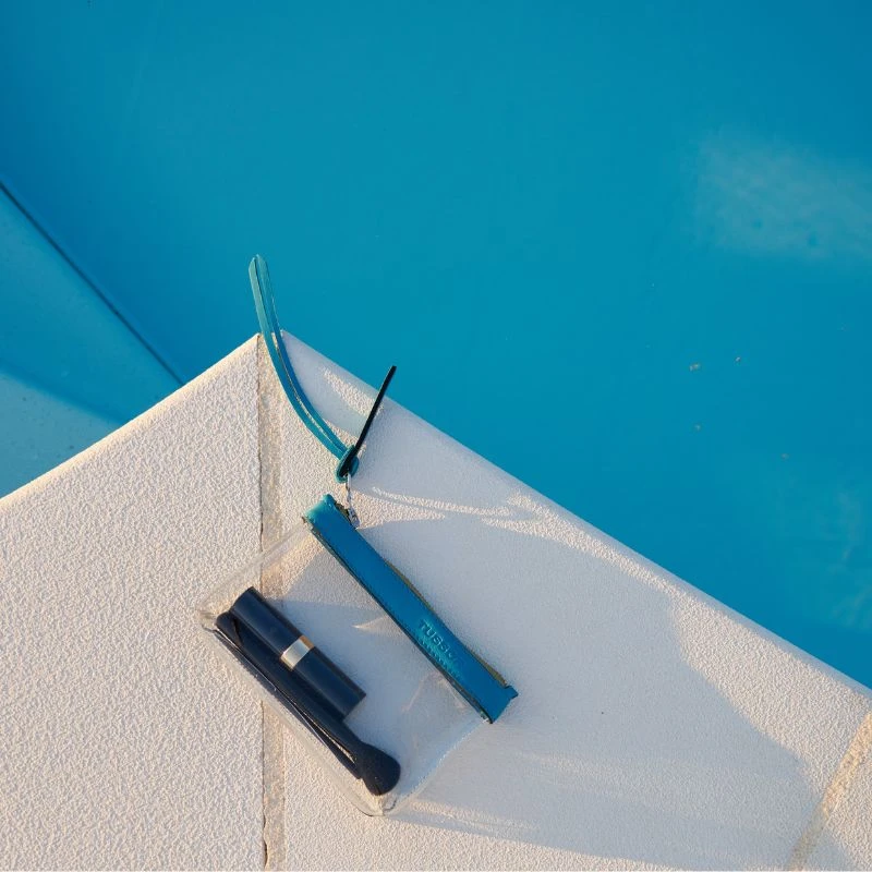 pochette en plastique transparent et cuir turquoise au bord d'une piscine
