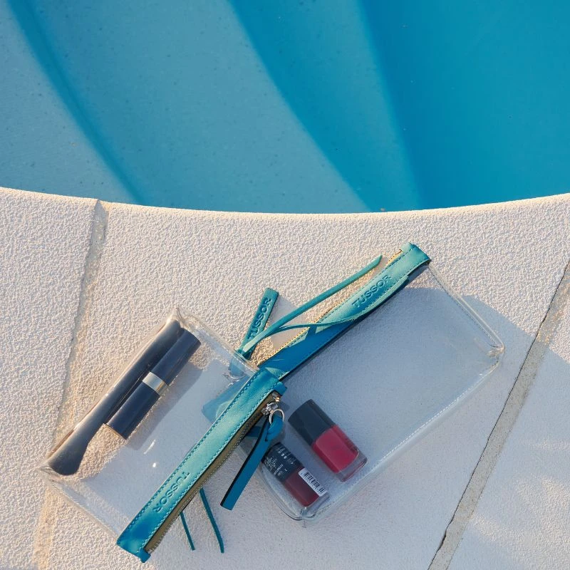 pochette en plastique transparent et cuir turquoise sur bord de piscine