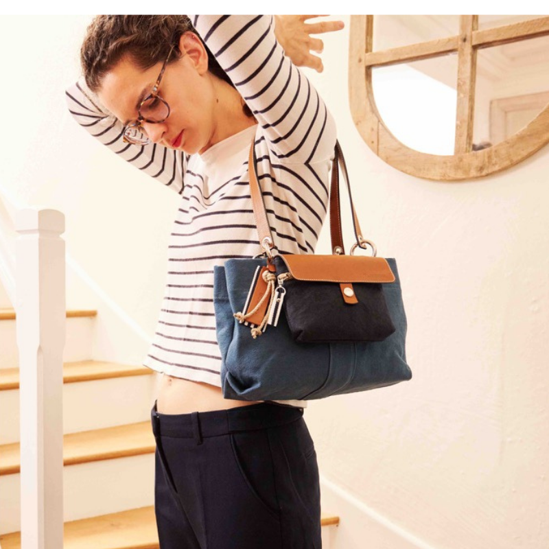 sac de ville modulable en coton bleu canard avec des anses en cuir naturel avec sa mobile marine tenu par ne femme en tee shirt marin